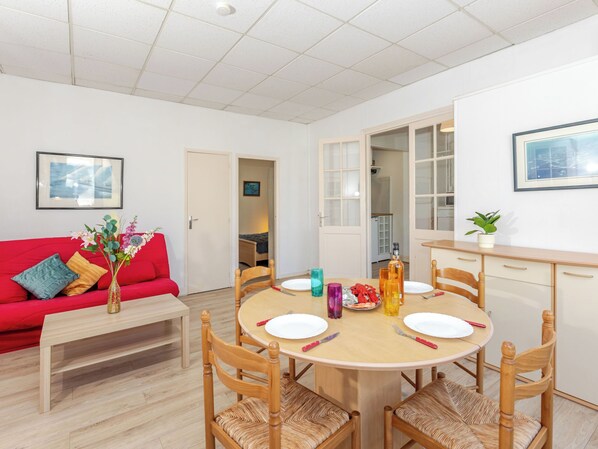 Ett modernt vardagsrum med en röd soffa, ett matbord i trä med stolar, ett litet soffbord och ett köksområde som syns genom en öppen dörr.