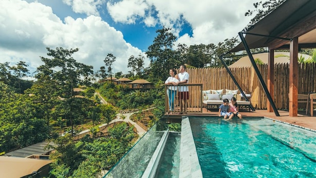 Una piscina con una barrera de vidrio, rodeada de abundante vegetación y una terraza de madera.