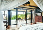 A bedroom with a large bed, a desk with a lamp, and a view of the outdoors through a sliding glass door.