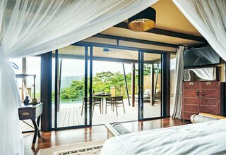 A bedroom with a large bed, a desk with a lamp, and a view of the outdoors through a sliding glass door.