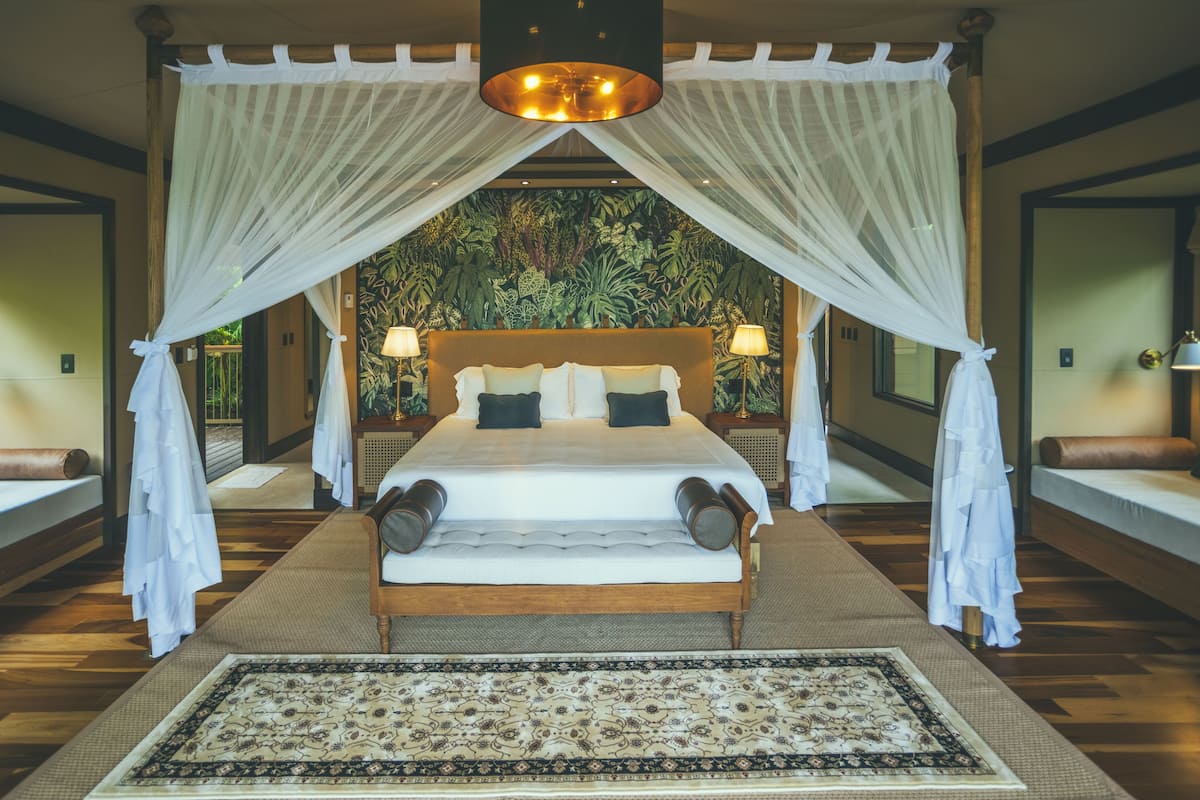 A large bed with a canopy, two bedside lamps, and a patterned rug.