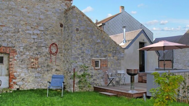 Een stenen gebouw met een gazon, een blauwe stoel, een tafel en een parasol.