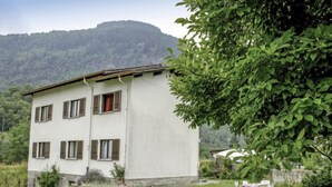 Un edificio a due piani con facciata bianca e persiane marroni, immerso in un prato e un giardino curati.