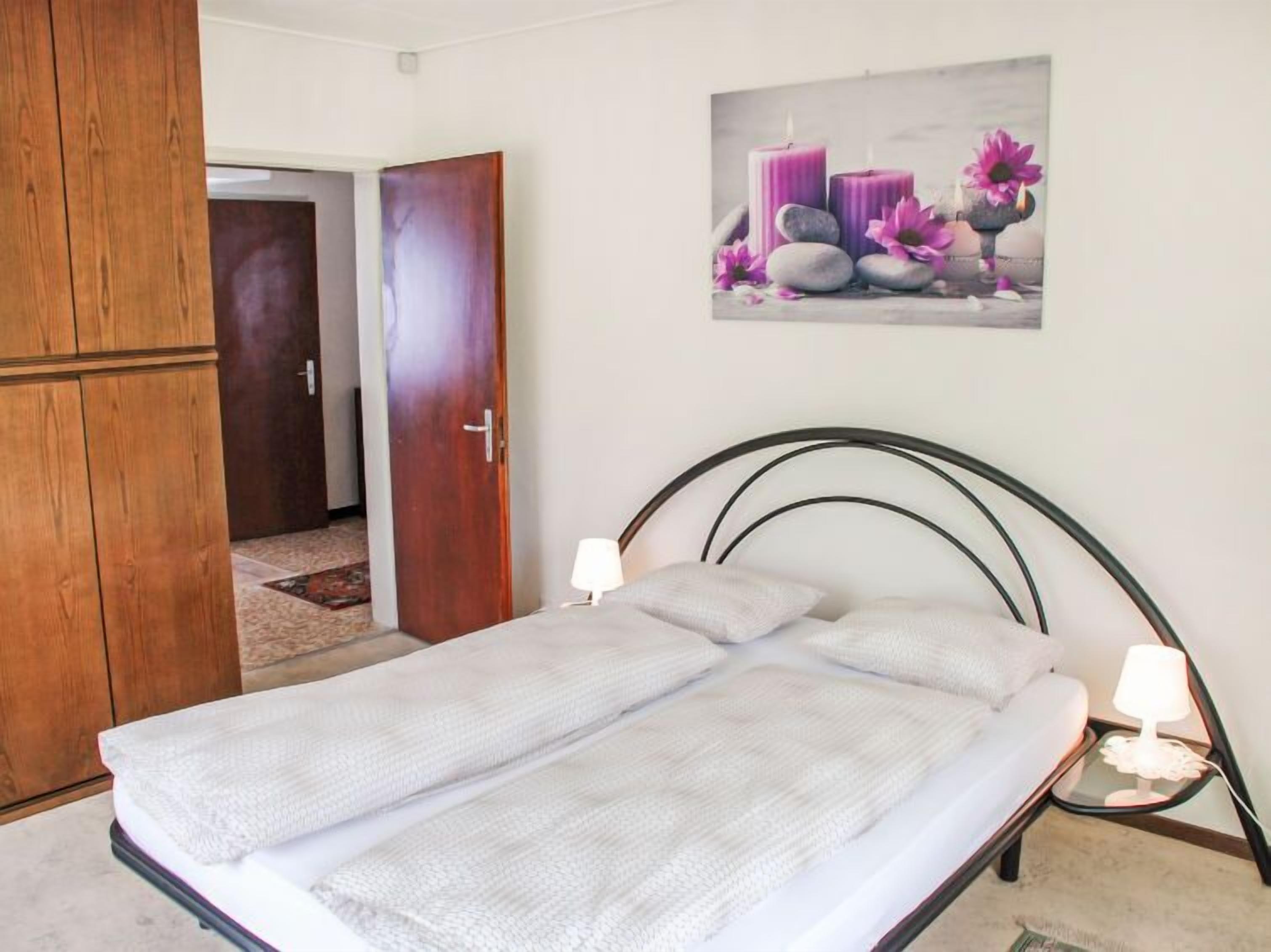 A bedroom with a bed, a wooden wardrobe, and a wall-mounted picture of candles and flowers.
