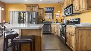 Una cocina con armarios de madera, electrodomésticos de acero inoxidable y una zona de bar con taburetes.