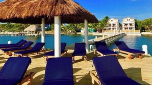 Un resort frente a la playa con una sombrilla de paja, sillas de descanso y piscina.