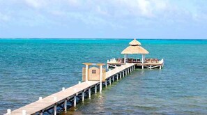 Une jetée mène à une structure à toit de chaume, dotée de sièges, et s’avance dans une mer turquoise.