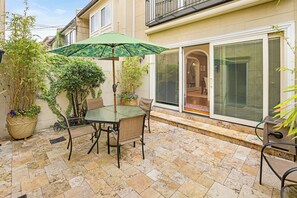 A patio with a glass table and chairs, a green umbrella, and potted plants. - Broughton Street Villa with Rooftop Terrace, Garage Parking by Lucky Savannah (Savannah)