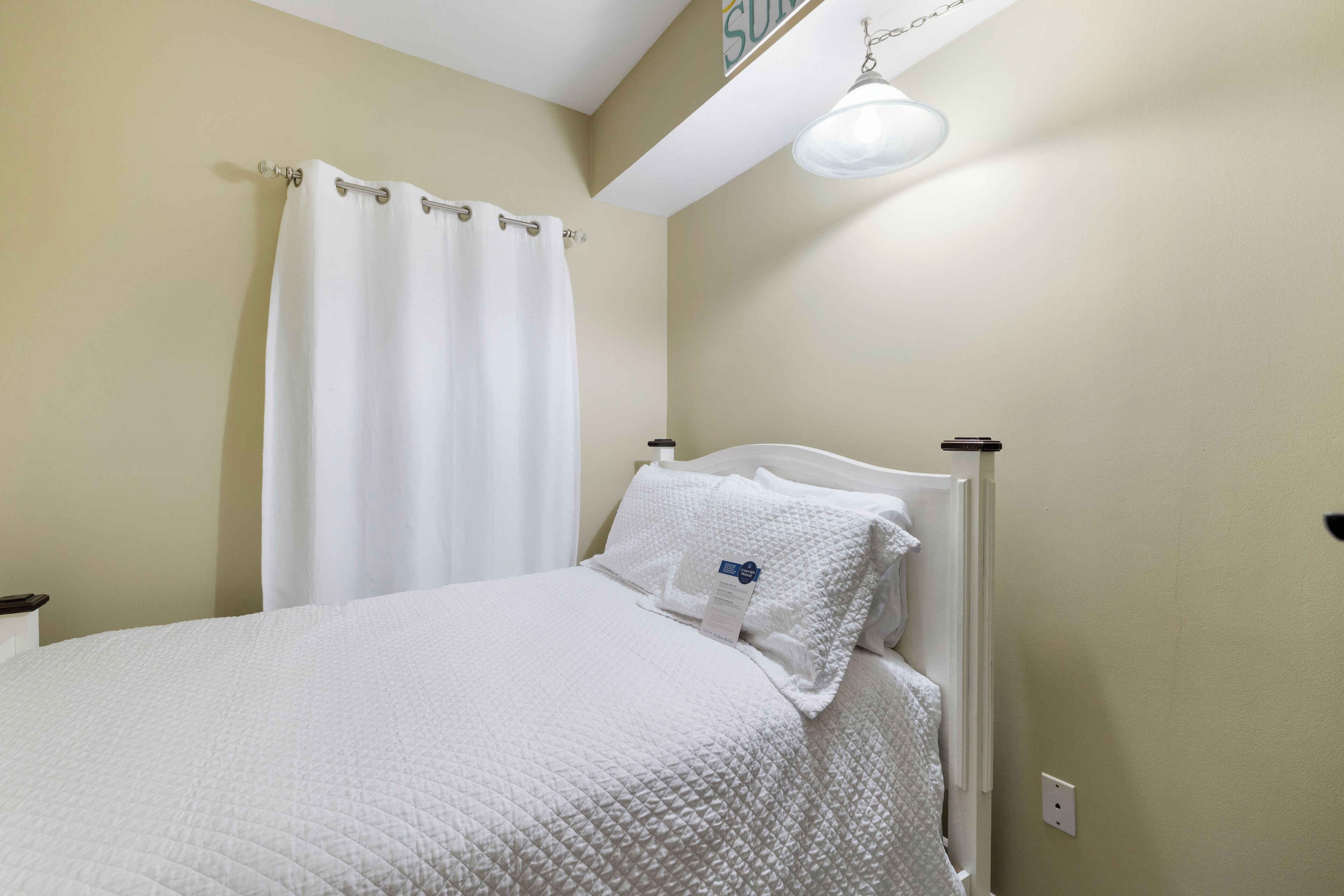 Una cama bien hecha con ropa de cama blanca, cabecera blanca y cortina blanca.