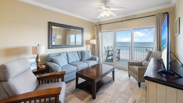 Een woonkamer met een bank, fauteuil, salontafel en een televisie. Er is een balkon met uitzicht op de oceaan.