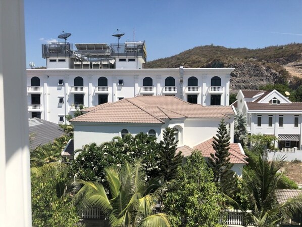A white building with a tiled roof, surrounded by greenery and a hilly landscape.