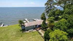 A lakeside property with a dock, a small house with a deck, and a grassy area.