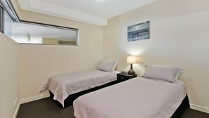 Habitación de hotel con dos camas, una mesita de noche, una lámpara, un cuadro y un tragaluz.