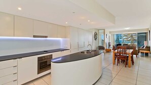 Cocina moderna con una isla central, horno empotrado y una zona de comedor con mesa y sillas.