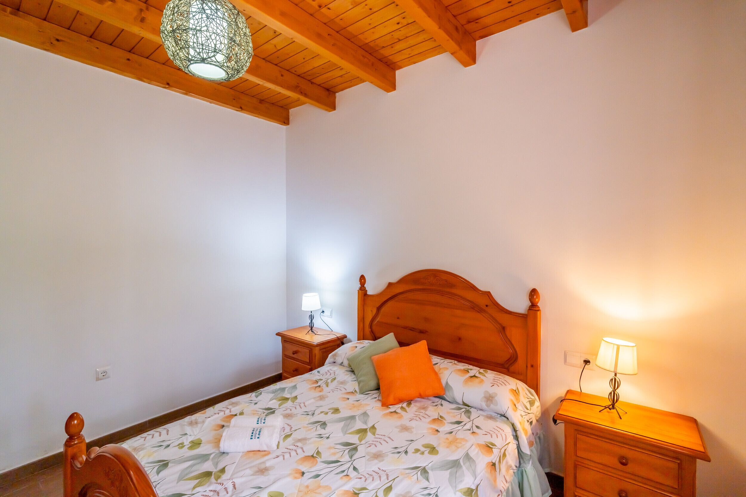 A bedroom with a wooden bed, a nightstand with a lamp, and a ceiling light fixture.