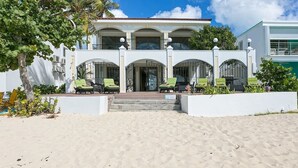 A beachfront property with a white building, a covered outdoor seating area with green chairs, and a palm tree. - Vittoria (6 bedrooms) - Beachfront villa, Simpson Bay, St. Maarten (Simpson Bay)