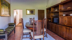 Uma sala de jantar com mesa e cadeiras de madeira, uma televisão sobre um móvel e um quadro na parede.