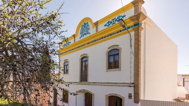 Um edifício com fachada branca, detalhes em amarelo e elementos decorativos azuis.