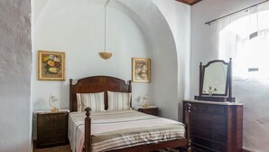 Quarto com cama de madeira, duas mesas de cabeceira, cômoda e duas pinturas penduradas na parede.