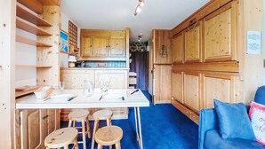 Eine kompakte Küche mit Holzausstattung, einer zentralen Kochinsel mit Sitzgelegenheiten und einem blau-vorgetieften Teppichboden.