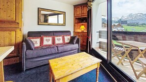 Ein gemütliches Wohnzimmer mit einer Couch, einem Holztisch, einem Spiegel und Blick auf einen Balkon mit Gartenmöbeln.