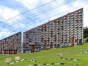 A modern multi-story residential building with a mix of balconies and windows, situated on a grassy slope with a clear sky. - Belleville Caron 1 - 1214 by Interhome (Les Menuires)