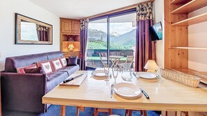 Ein gemütliches Zimmer mit einer Couch, einem Esstisch für vier Personen und einem großen Fenster mit Blick auf die Berge.