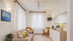 Une chambre à coucher avec un lit, une table de chevet, une chaise, un téléviseur et une fenêtre avec des rideaux.