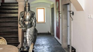 Ein Gang mit einer Statue eines Ritters aus dem Mittelalter, einer Treppe und einem Fenster mit Tageslicht.