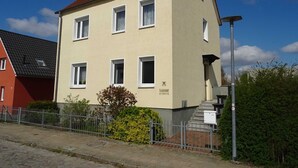 Ein zweistöckiges Gebäude mit rotem Ziegeldach, zahlreichen Fenstern und einem kleinen Vorgarten.