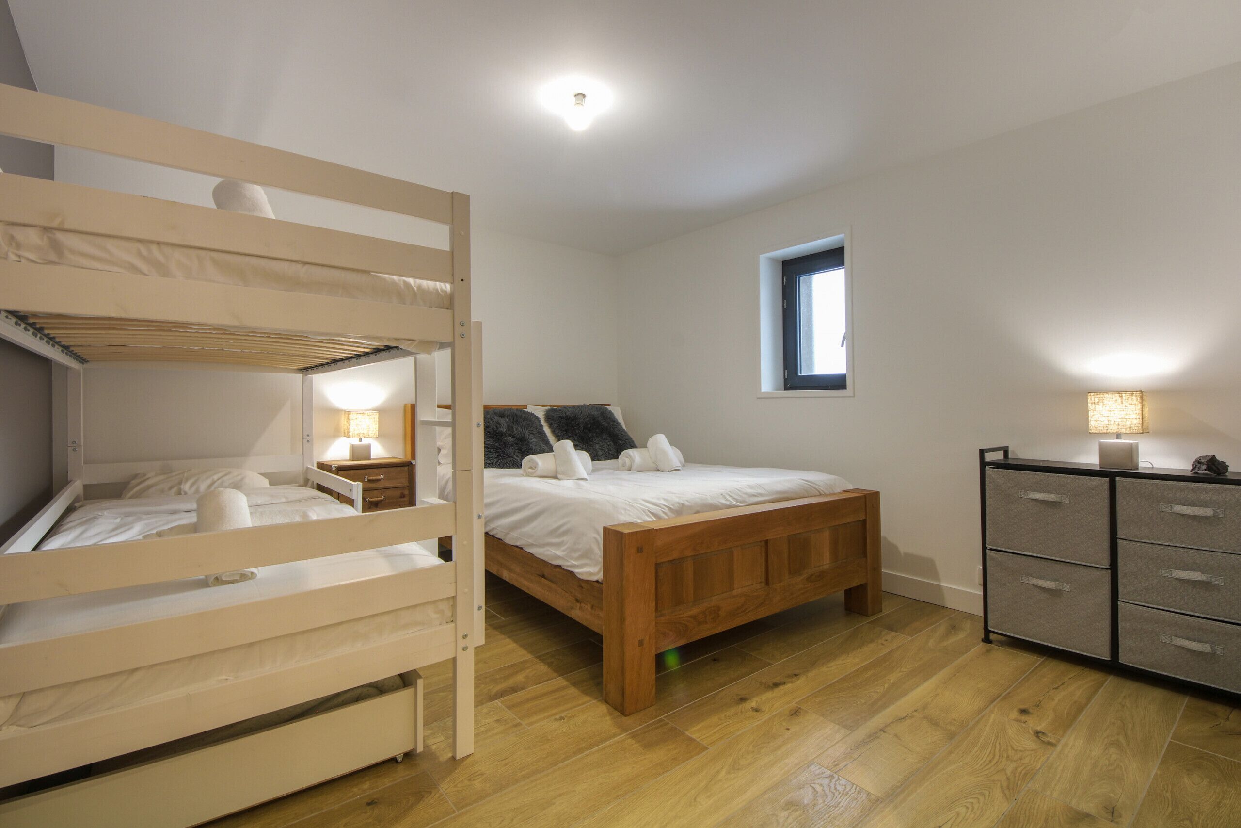 A bedroom with a bunk bed, a single bed, a dresser, and a window.