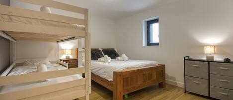 Un dormitorio con una cama litera, una cama individual, un aparador y una ventana.
