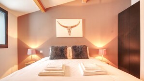 A neatly made bed with folded towels, two fluffy pillows, and a wall-mounted artwork of a bull's head. - Maison des Praz (Chamonix-Mont-Blanc)