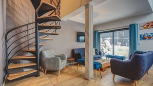 A modern living room with a spiral staircase, two sofas, and a large window with a view of the outdoors. - Maison des Praz (Chamonix-Mont-Blanc)