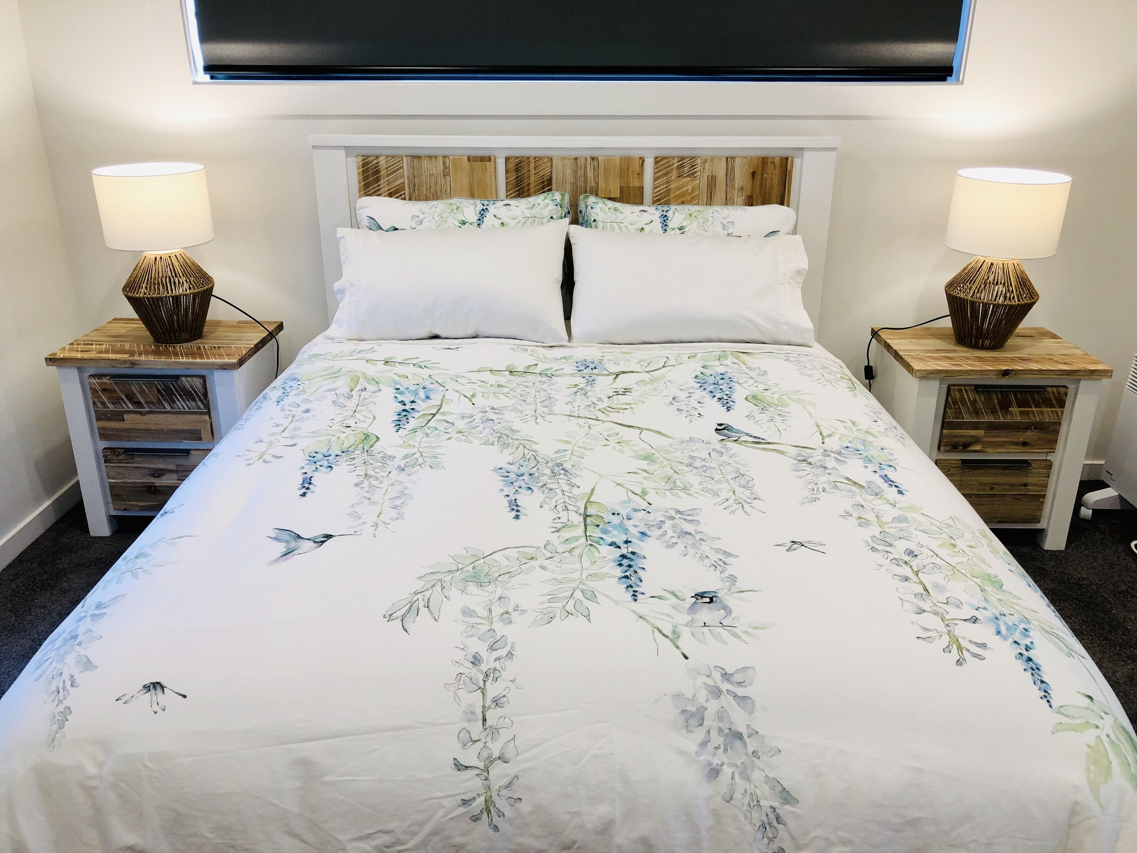 Uma cama com colcha florida, duas mesas de cabeceira com abajures e uma cabeceira de madeira.