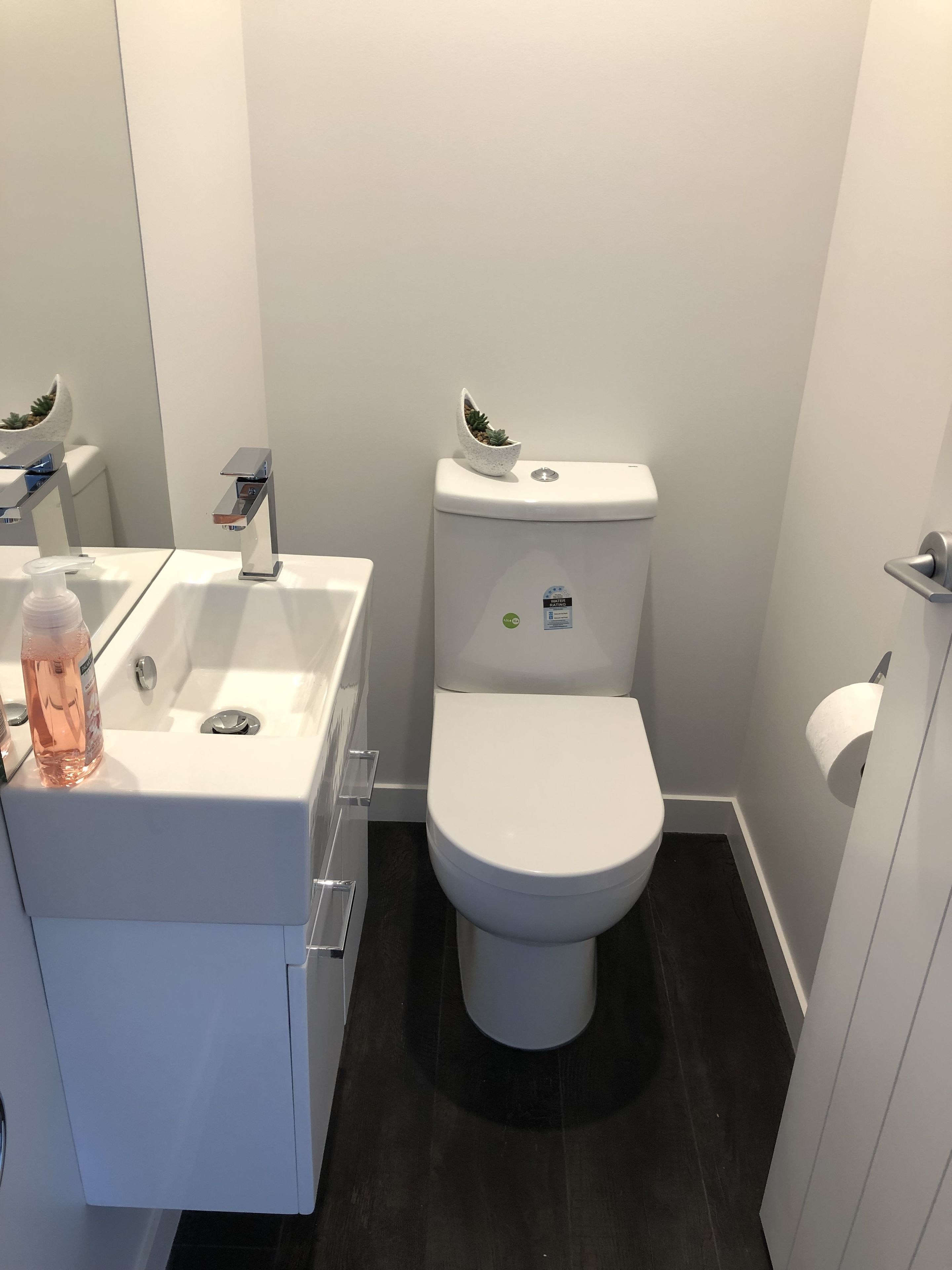 Un baño moderno con un lavamanos blanco, un inodoro y una pequeña planta en maceta sobre el tanque.