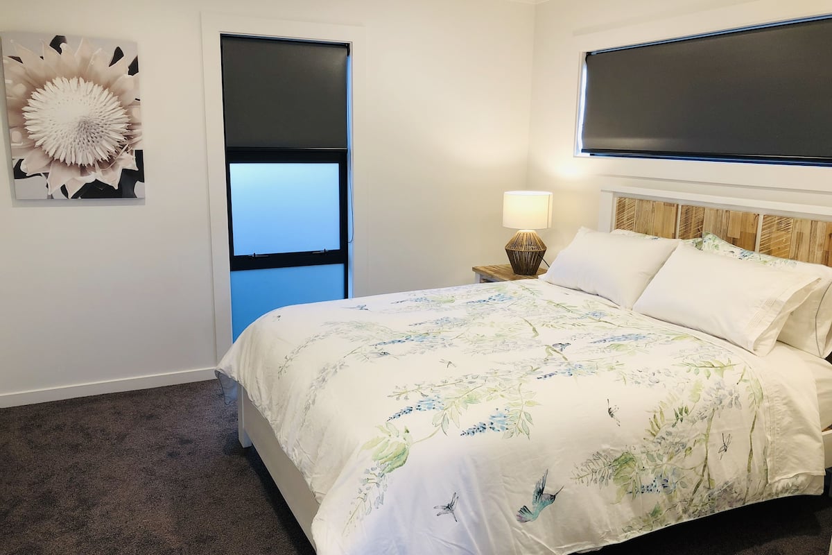 A bedroom with a bed, a nightstand, a lamp, a wall-mounted TV, and a door.
