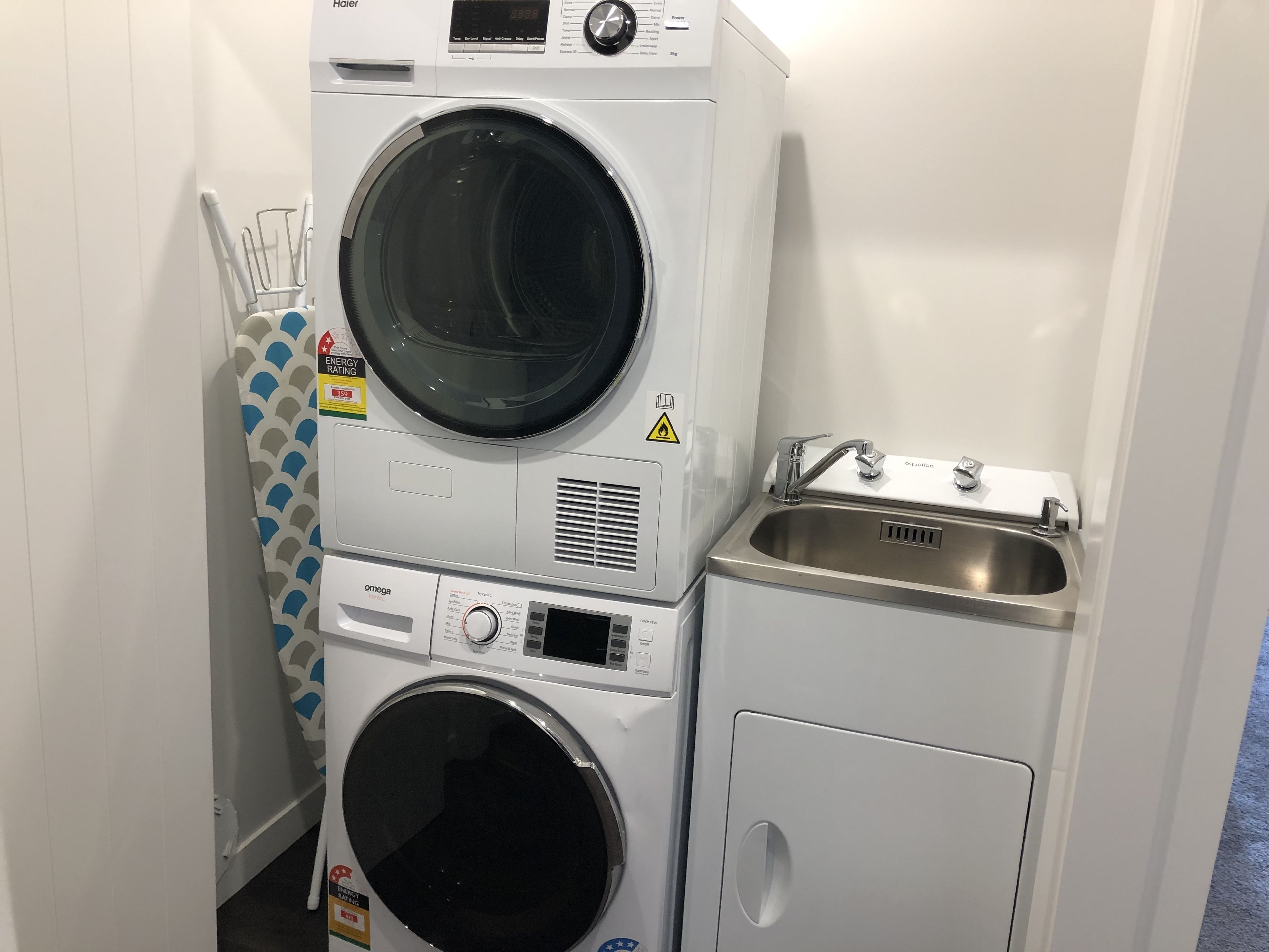 A compact laundry area with a front-loading washer, a stacked dryer, and a sink.