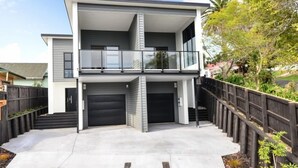 A modern two-story house with a balcony, a garage, and a fenced backyard. - Central Park Gemini Apartments (Hamilton)