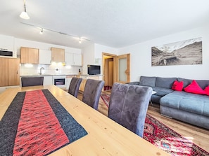 A modern living space with a dining area, kitchen, and a sofa with red cushions.