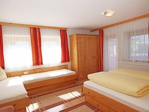 A room with two beds, wooden walls, and large windows with red curtains.