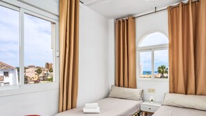 Une chambre d’hôtel avec deux lits, un petit tabouret et une fenêtre avec des rideaux.
