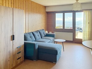 Ein modernes Wohnzimmer mit einer Eckcouch, einem kleinen runden Tisch und Blick durch große Fenster.