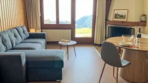 Una sala moderna con un sofá, una mesita, una mesa de comedor con sillas, vistas al exterior a través de ventanas grandes y una chimenea.