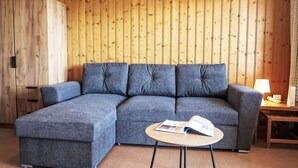 Una sala de estar moderna con un sofá seccional, una mesita redonda con una revista y una lámpara sobre una mesita auxiliar de madera.
