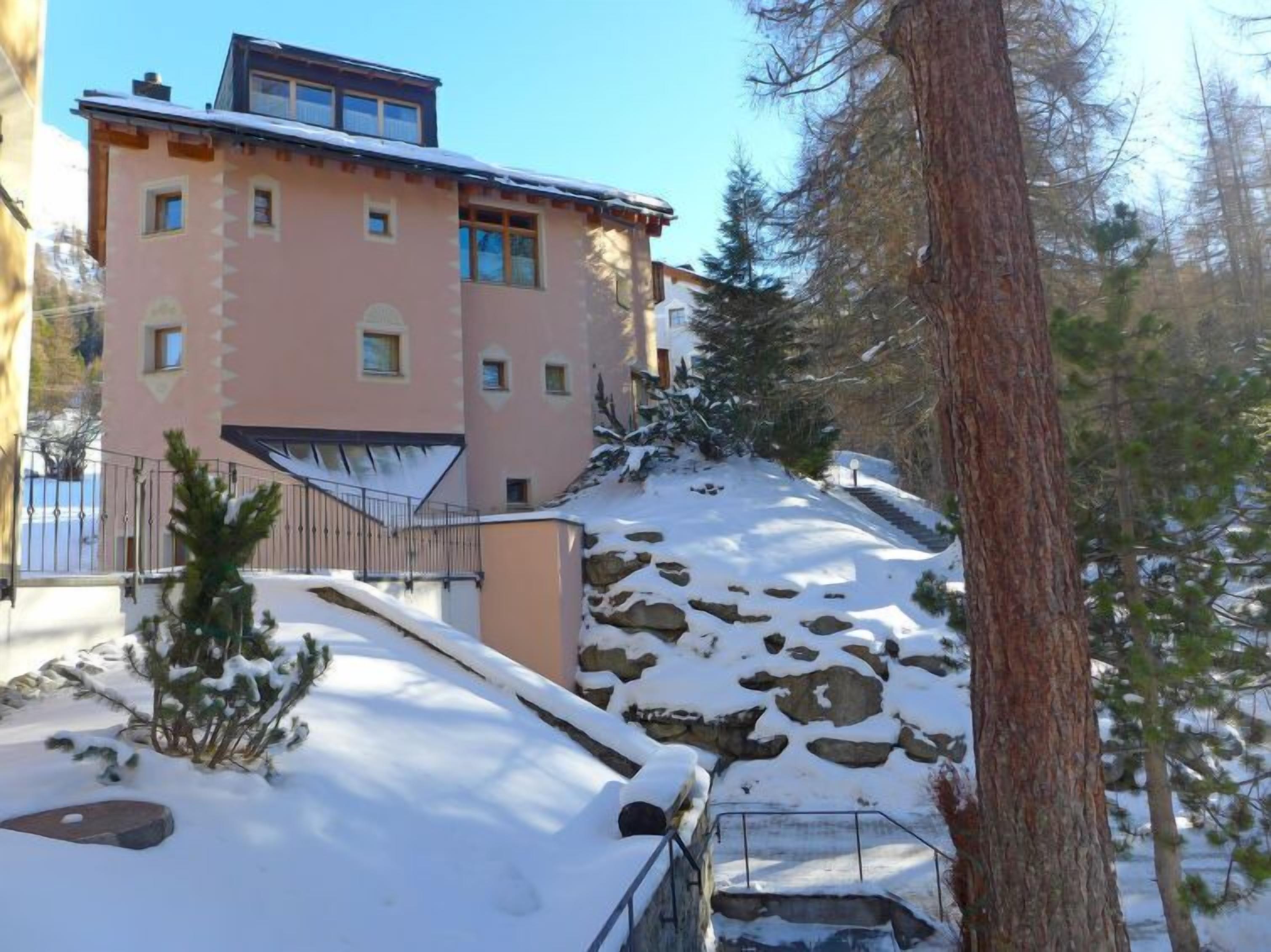 A multi-story building with a sloped roof, surrounded by snow-covered ground and trees.