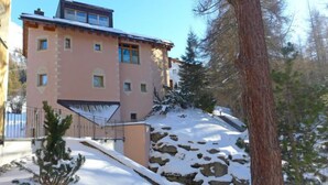 Un edificio de varios pisos con techo inclinado, rodeado de terreno y árboles cubiertos de nieve.
