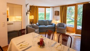 Un comedor con una mesa dispuesta para dos personas, un sofá gris y una cocina al fondo.