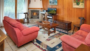 Ein gemütliches Wohnzimmer mit Kamin, roten Sofas, einem Holztisch und einem Fernseher.