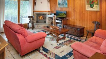 Un salon chaleureux avec une cheminée, des canapés rouges, une table basse en bois et un téléviseur.